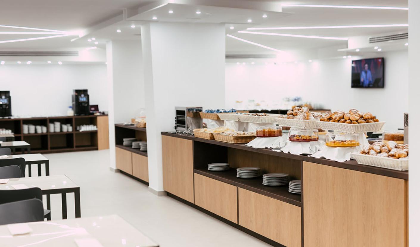 Sala colazioni moderna con buffet di dolci e tavoli apparecchiati.