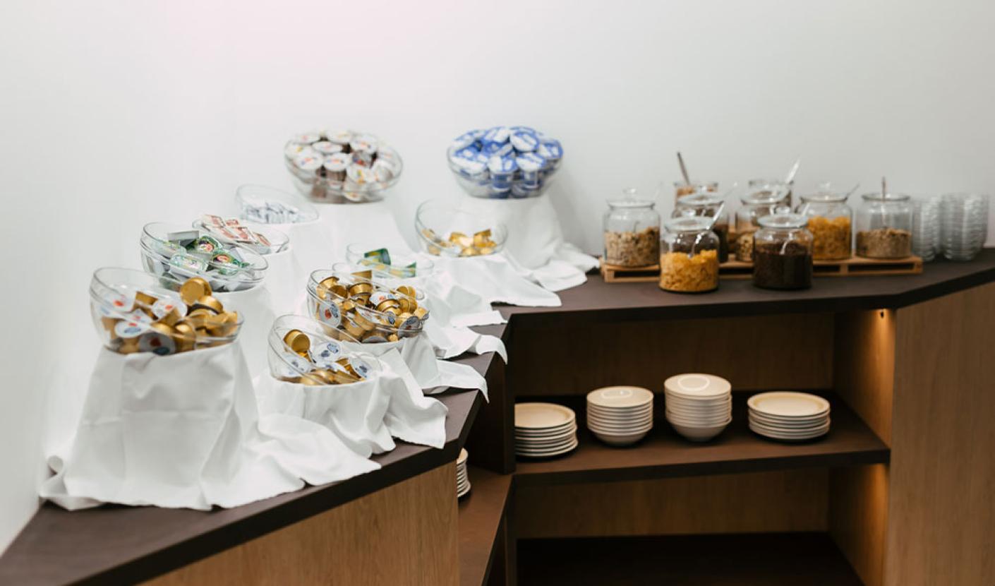 Buffet con cereali, yogurt e piatti su scaffali in legno.