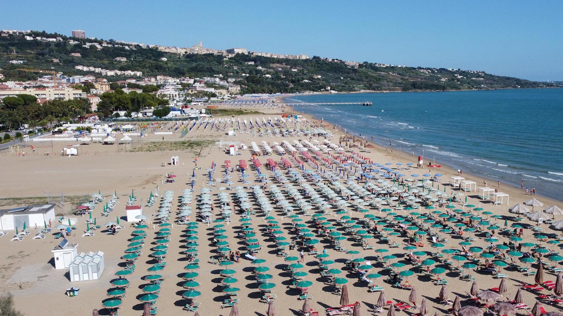 Spiaggia affollata con ombrelloni colorati e mare calmo, vista panoramica.