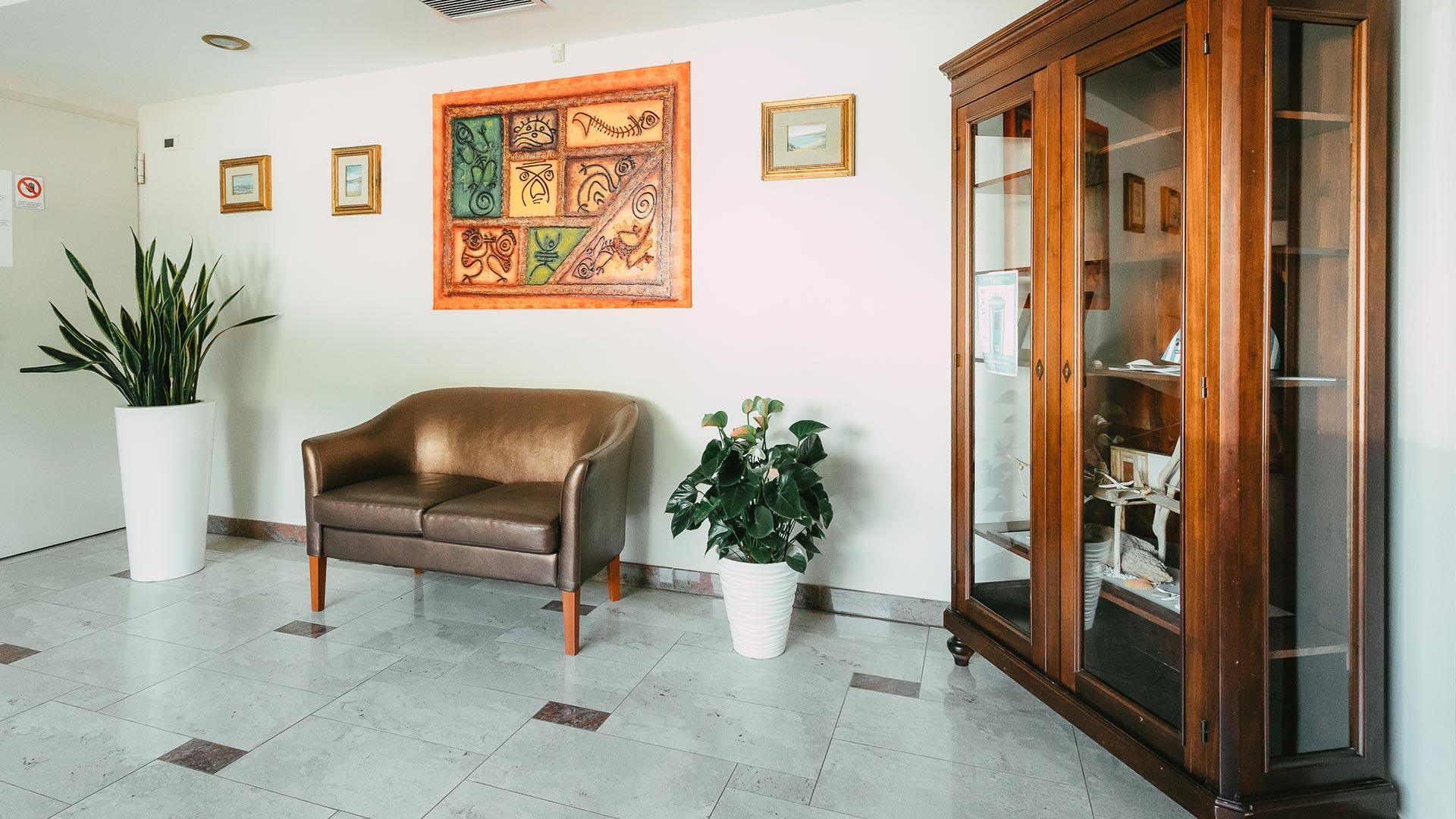 Waiting room with a sofa, plants, a display cabinet, and colorful paintings.