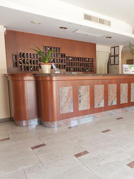 Reception di un hotel con bancone in legno e pianta decorativa.
