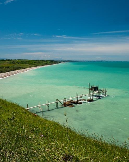Spiaggia con mare turchese e un molo di legno su una costa verde.