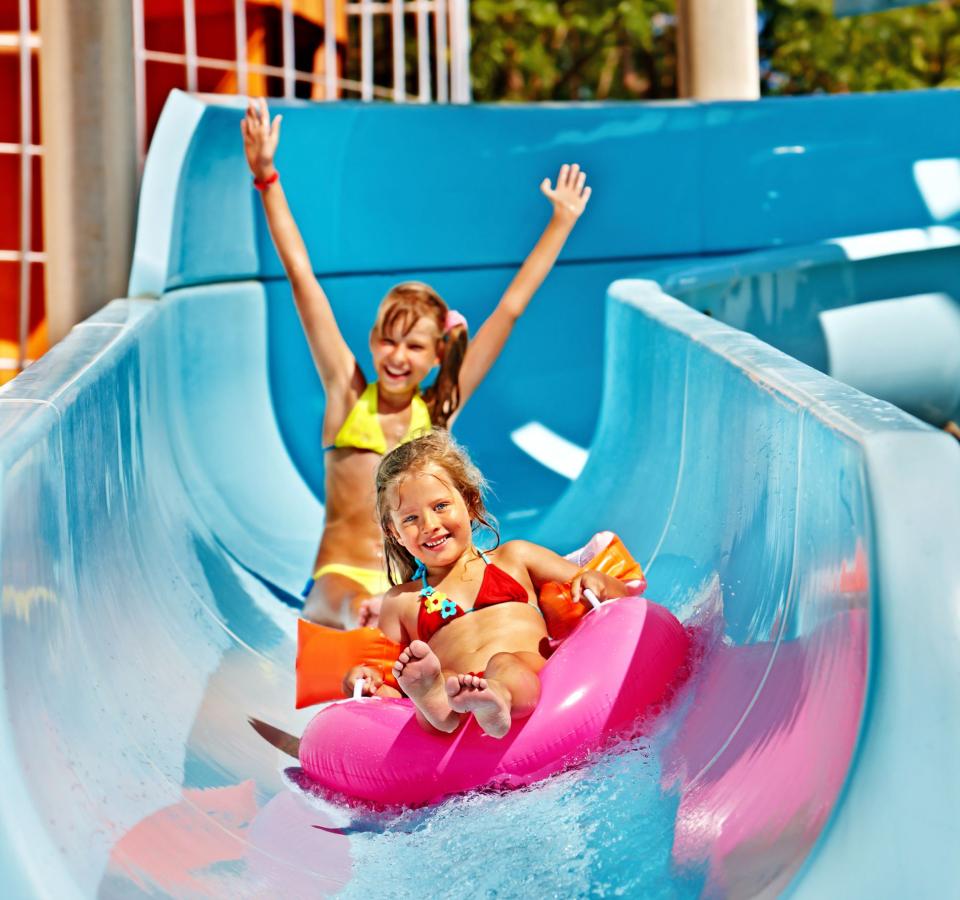 Happy kids sliding on a waterslide with a pink float.