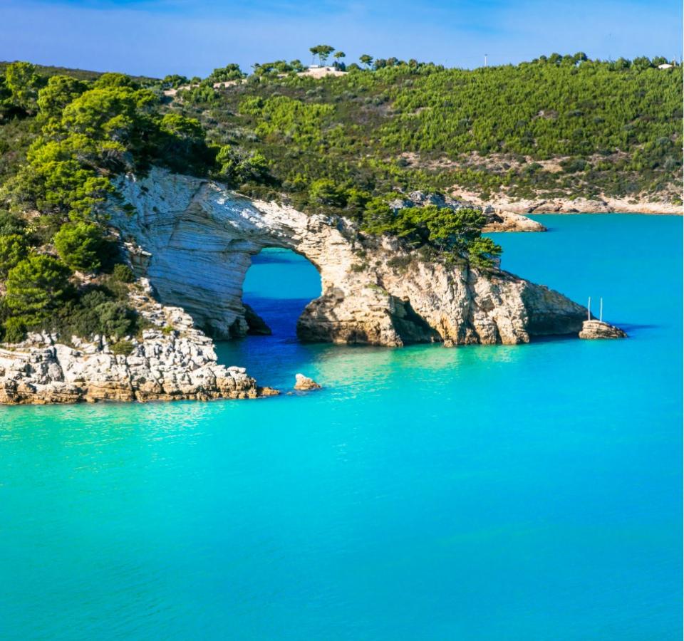 Natural arch over turquoise waters, surrounded by lush vegetation.