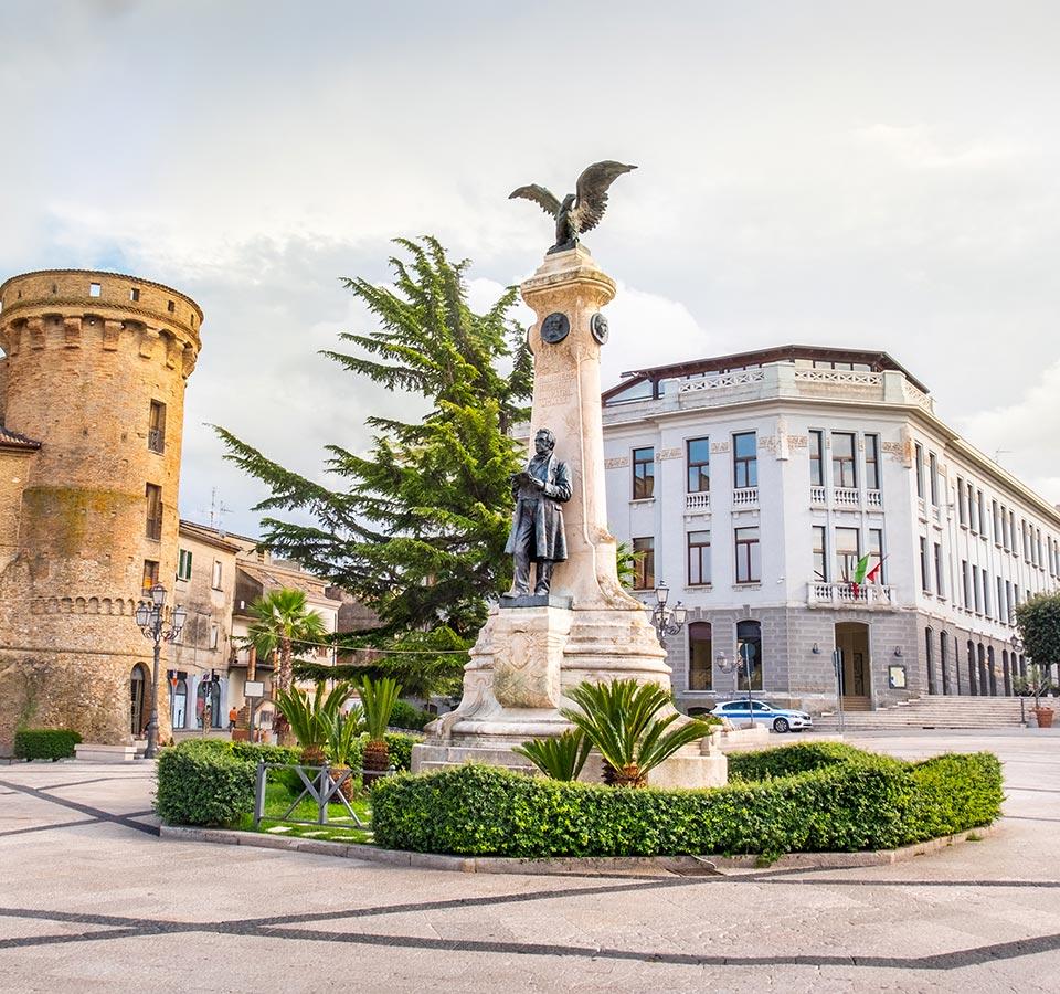 Square with monument, medieval tower, and historic building in an Italian city.