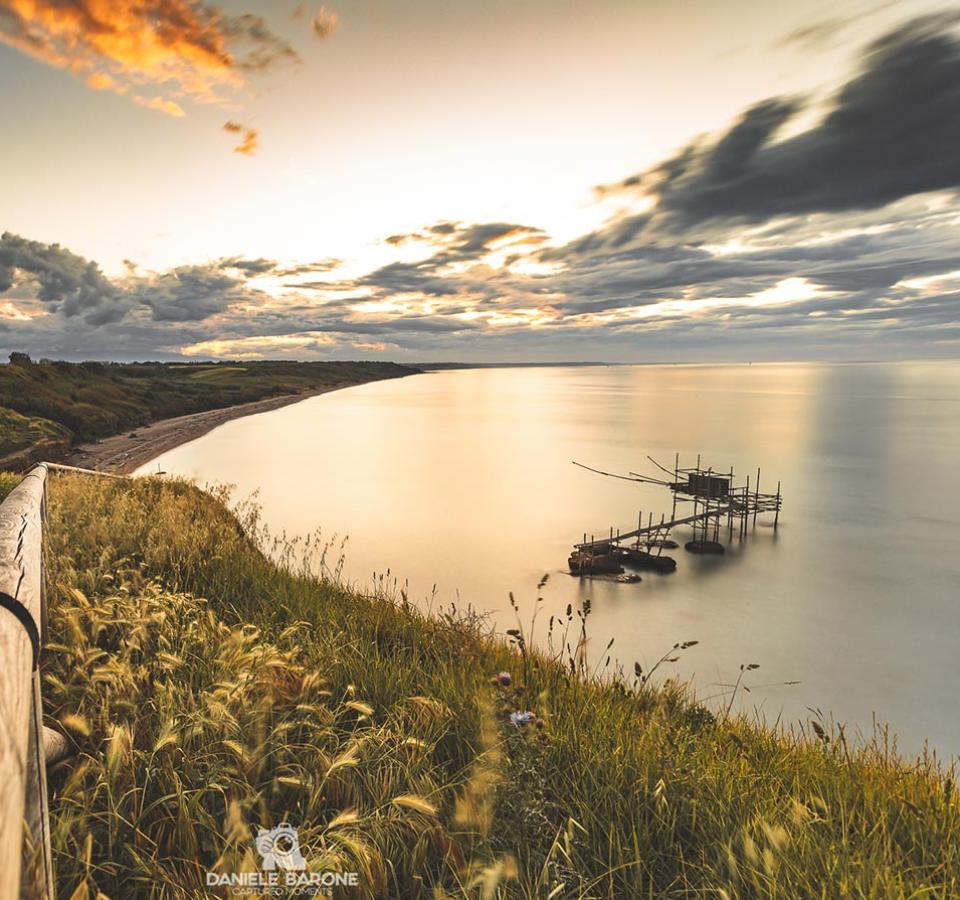 Sunset over a green coast with a trabocco on the calm sea.