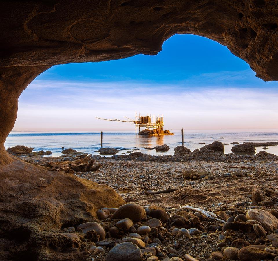 View of a trabocco through a cave on the rocky coast.