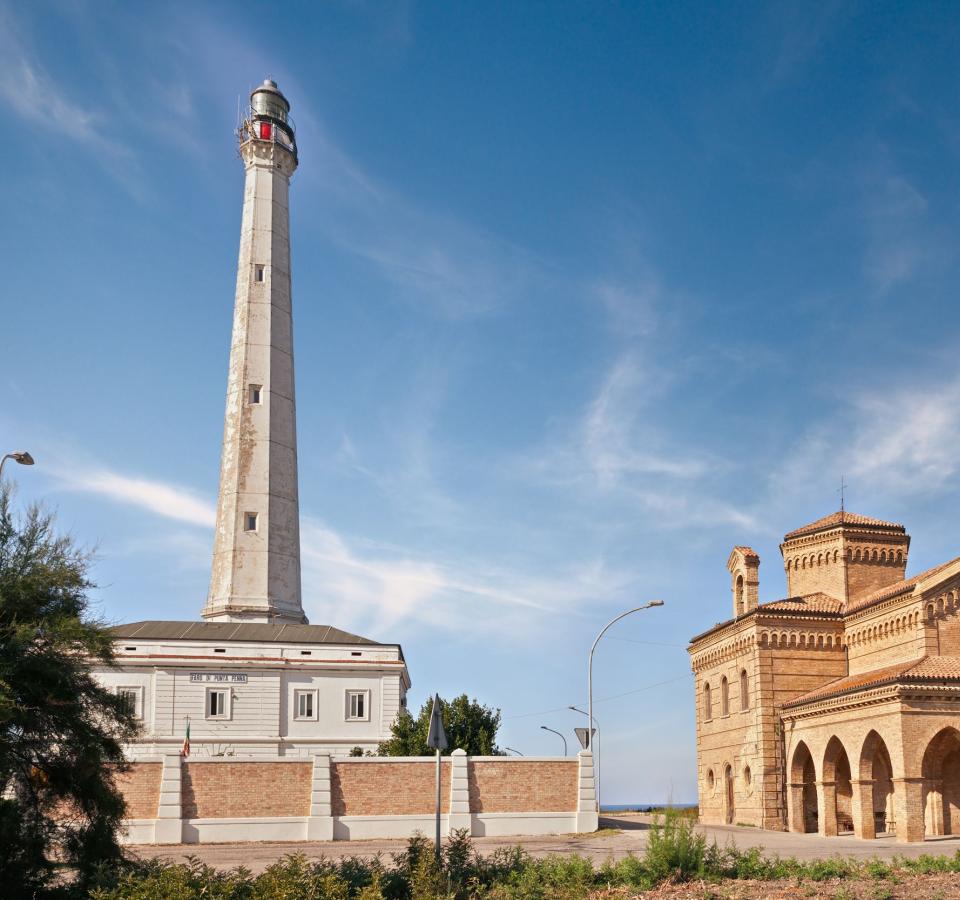 Lighthouse and historic church under a blue sky, near the sea.