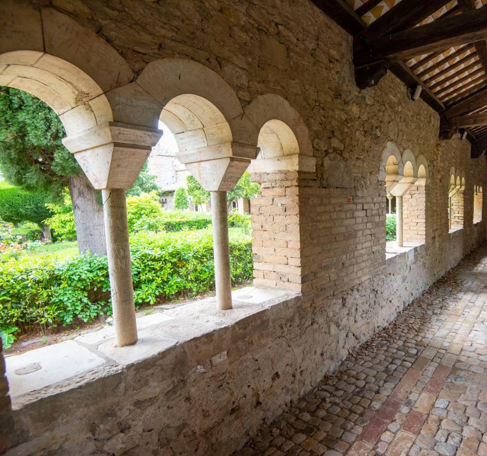 Medieval cloister with stone arches and cobblestone floor.