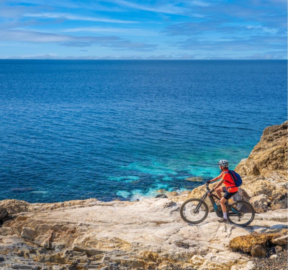 Cyclist on rocky cliff with a view of the blue sea.